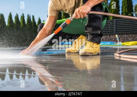 Les hommes caucasiens lavant sa piscine composite fait terrasse à l'aide de tuyau d'eau. Tâche d'entretien de cour arrière. Banque D'Images