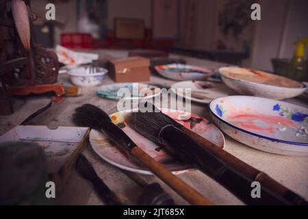 Pinceaux d'un artiste chinois debout sur la table dans une assiette avec d'autres peintures à l'huile autour Banque D'Images