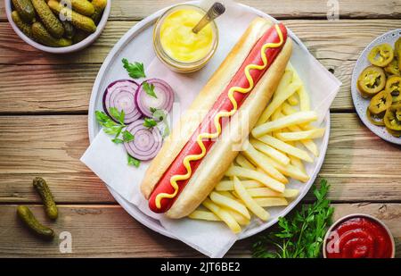 Hot dog servi avec des frites, des cornichons Gherkin, des tranches de jalapeno, des oignons frais, du persil frais, moutarde au miel et ketchup. Vue de dessus avec gros plan. Banque D'Images