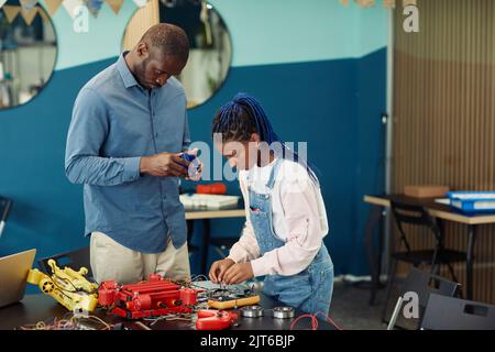 Portrait d'un enseignant de sexe masculin aidant une jeune fille afro-américaine à construire un robot pendant la classe d'ingénierie à l'école, dans l'espace de copie Banque D'Images