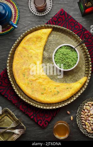 Cuisine arabe : pâtisseries traditionnelles du Moyen-Orient et célèbre dessert du Ramadan « Kunafa » servi avec des pistaches écrasées, du sirop de miel et une tasse de thé. Banque D'Images