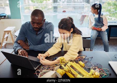 Portrait d'une jeune fille adolescente construisant des robots en classe d'ingénierie avec l'aide d'un enseignant masculin Banque D'Images