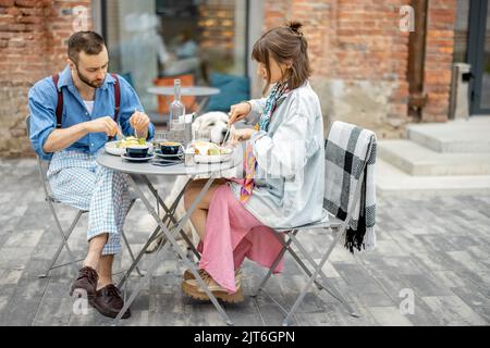 Un homme et une femme élégants ont un petit déjeuner tout en étant assis avec un chien dans un café à l'extérieur Banque D'Images