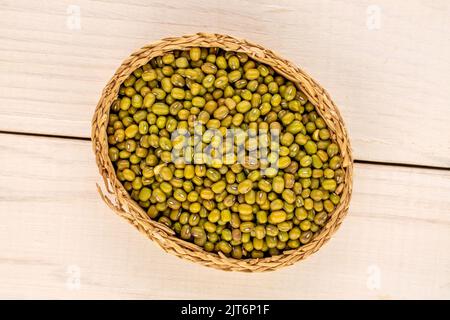 Beaucoup de haricots mung bio non cuits dans un bol de paille sur une table en bois, vue rapprochée, vue de dessus. Banque D'Images