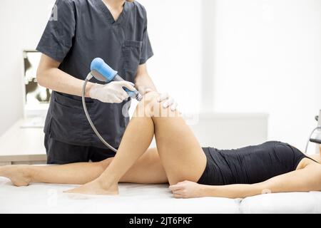 Le médecin applique un traitement par onde de choc sur le genou des femmes Banque D'Images