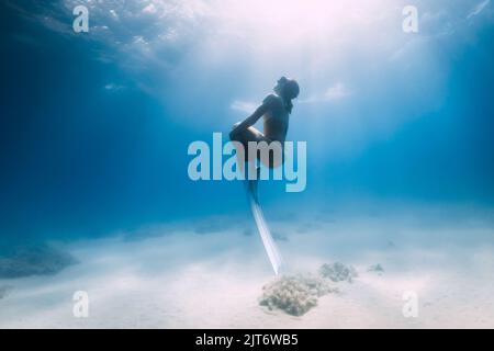 Lady frediver en bikini posant sous l'eau sur fond de mer sablonneux avec des ailerons. Femme attrayante sur les profondeurs de l'océan bleu Banque D'Images
