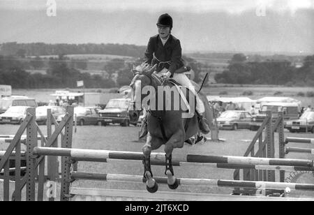 1980s, une jeune femme a fait un saut à cheval sur une clôture lors d'un spectacle de comté, Yorkshire, Angleterre, Royaume-Uni. Le saut de spectacle est un événement équestre où le cavalier et le cheval tentent de sauter sur toutes les clôtures sur un parcours, sans les frapper et dans un délai défini. Banque D'Images