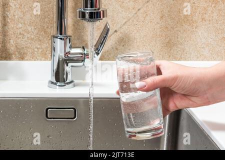 Eau d'un robinet dans un verre tenu par la main d'une femme Banque D'Images