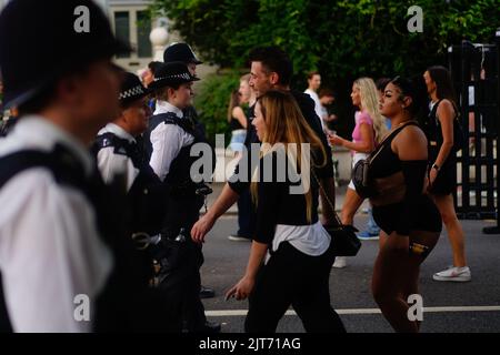 Les amateurs de carnaval traversent une ligne d'officiers de police qui ont été à l'origine de détecteurs de métaux pendant la journée de famille au Notting Hill Carnival de Londres, qui est retourné dans la rue pour la première fois deux ans après avoir été contrecarré par la pandémie. Date de la photo: Dimanche 28 août 2022. Banque D'Images