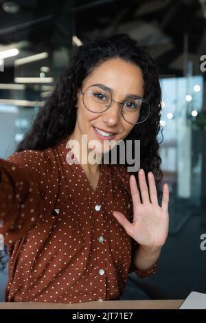 Photo verticale, jeune femme d'affaires hispanique aux cheveux bouclés qui parle lors d'un appel vidéo, agitant la caméra du smartphone, à l'aide d'une application de communication à distance Banque D'Images