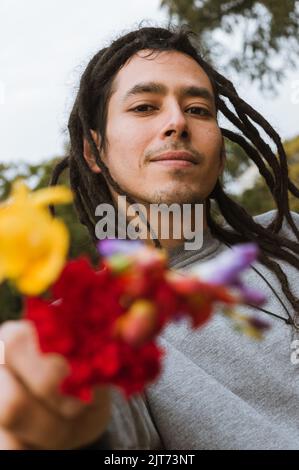 portrait vertical du jeune latin vénézuélien, plein air souriant pointant vers l'appareil photo avec des fleurs. Banque D'Images