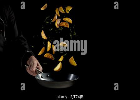 Un chef en uniforme, en cuisant de délicieuses pommes de terre coupées et des herbes en friture avec copyspace Banque D'Images