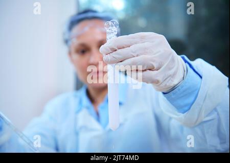 Tube à essai sur fond flou de scientifique pharmacologue examinant la réaction chimique en cours en laboratoire Banque D'Images