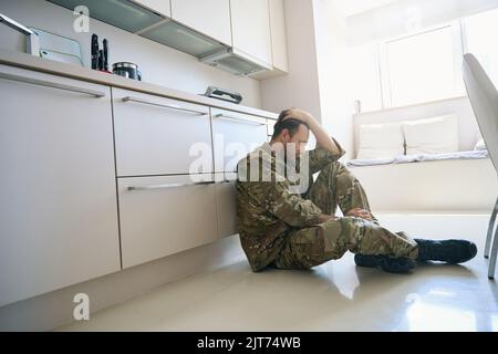 Un militaire contrarié en posture de deuil est assis sur le sol Banque D'Images