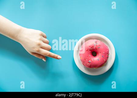 Faire un donut avec du glaçage rose et une main femelle sur fond bleu. Banque D'Images