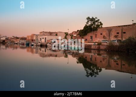 Le soleil se lève au port de Mazara del Vallo en Sicile. Le ciel se reflète dans l'eau. Les maisons bordent le bord du port et les bateaux sont amarrés le long Banque D'Images