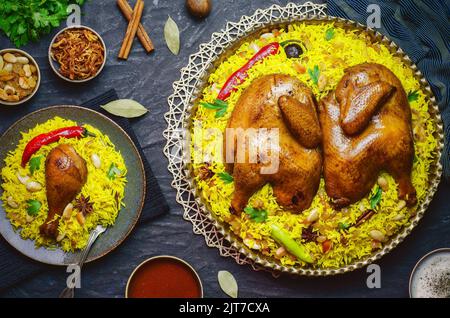 Cuisine arabe; poulet 'Kabsa' ou poulet Beryani riz. Servi avec des oignons frits dorés, des noix grillées croustillantes, du raisin sec et du persil frais. Banque D'Images