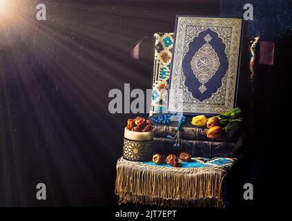 Le Saint-Livre islamique 'Coran' entouré de rayons lumineux et placé avec des perles rosaires, des dattes fraîches, des fleurs de tulipe et un tapis de prière sur une chaise en bois. Banque D'Images