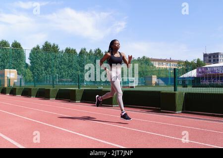 Faites participer la jeune femme noire aux courses de sport sur la piste rouge du stade de la ville, en vue des compétitions Banque D'Images