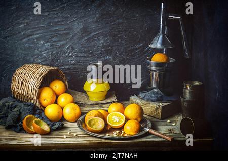 Classique encore vie avec des oranges fraîches placées avec de vieux presse-fruits en métal sur fond rustique en bois. Banque D'Images