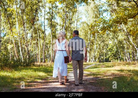 Couple familial senior marchant à l'extérieur dans la forêt d'été. Les personnes âgées tiennent les mains. Date romantique Banque D'Images