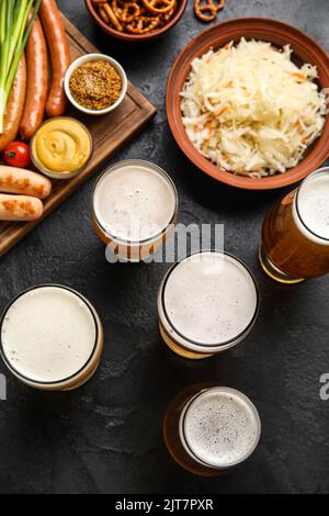 Grandes tasses de bière fraîche et de plats traditionnels sur fond sombre. Fête de l'Oktoberfest Banque D'Images