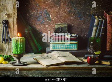 Classique encore la vie avec des livres vintage placés avec une bougie éclairée, de vieilles boîtes, pipe, clés anciennes, citron, menthe et boisson sur fond rustique en bois. Banque D'Images