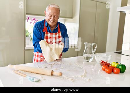 Homme âgé souriant confiant tenant la pâte avec les mains dans la cuisine Banque D'Images