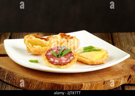 Gougères avec fromage et saucisse sur plaque blanche et table en bois Banque D'Images