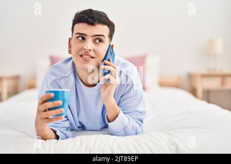 Jeune homme non binaire parlant sur le smartphone buvant du café Banque D'Images