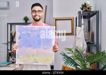 Jeune artiste homme arabe souriant confiant tenant dessiner à l'atelier d'art Banque D'Images