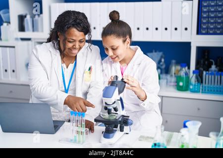 Mère et fille scientifiques utilisant un microscope et un ordinateur portable travaillant en laboratoire Banque D'Images