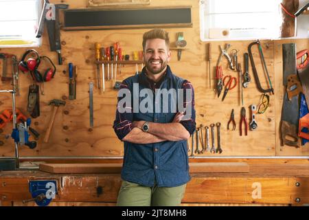 Laissez-moi le construire pour vous. Portrait d'un beau jeune homme debout avec ses bras pliés dans un atelier. Banque D'Images