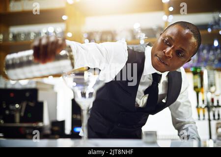 Il fait les meilleurs cocktails. Un barman bien habillé debout derrière le comptoir. Banque D'Images