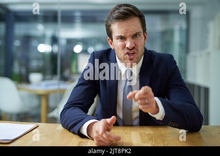 Vous avez tiré. Portrait d'un homme d'affaires en colère criant et pointant son doigt tout en étant assis à un bureau. Banque D'Images