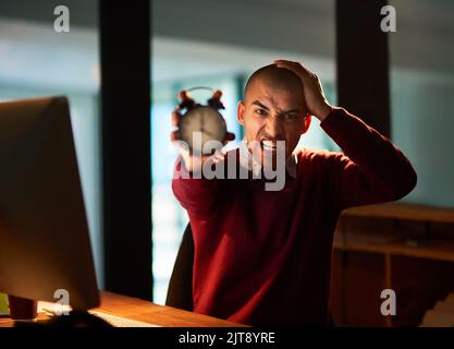 Mi à court de temps. Portrait d'un jeune homme qui frise le temps tout en travaillant tard dans son bureau. Banque D'Images