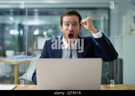 Ce travail est inacceptable. Portrait d'un homme d'affaires en colère criant et agitant un poing assis à son ordinateur portable sur un bureau. Banque D'Images