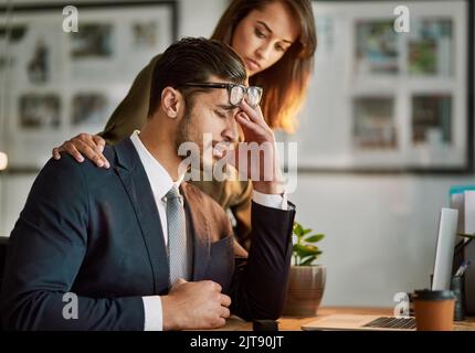 Trop de pression. Un homme d'affaires stressé étant réconforté tout en étant assis à une table à l'aide d'un ordinateur portable. Banque D'Images