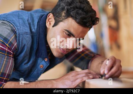 Des mesures exactes font toute la différence. Un homme de main concentré mesurant un morceau de bois tout en travaillant dans son atelier. Banque D'Images