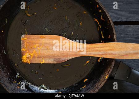 une poêle avec les restes de nourriture et une spatule en bois après la friture est sur la table dans la cuisine, une poêle sale est sur la table Banque D'Images