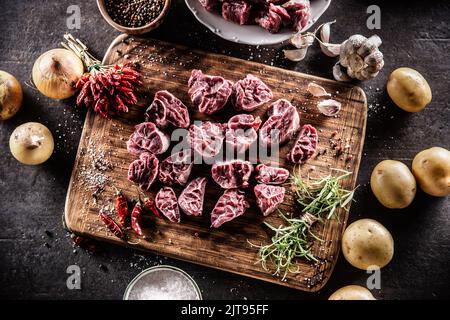 Tiges de boeuf cru coupées en petits morceaux placés sur une planche de bois avec d'autres ingrédients pris du dessus. Banque D'Images