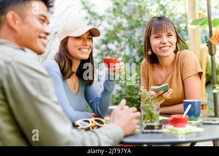 Des amis insouciants assis à table avec des tasses de café et bavardant entre eux dans un café extérieur Banque D'Images