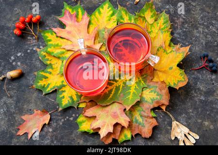 Deux mugs de thé chaud à la grenade avec des feuilles d'automne et des baies vives sur un fond de table grundy. La vie tranquille de l'automne. Banque D'Images