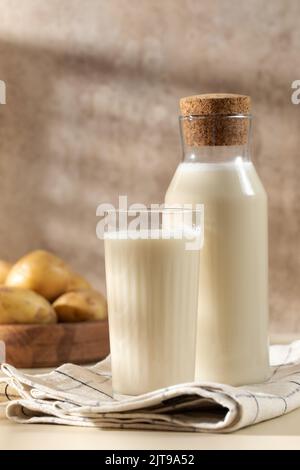 Un verre et un pot de lait de pomme de terre avec des pommes de terre crues dans un bol. Banque D'Images