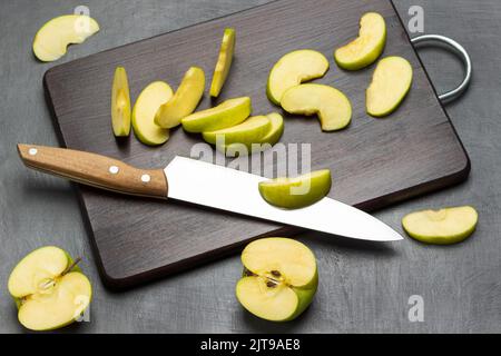Deux moitiés de pomme verte. Couteau de cuisine et tranches de pomme sur la planche à découper. Pose à plat. Arrière-plan gris. Banque D'Images
