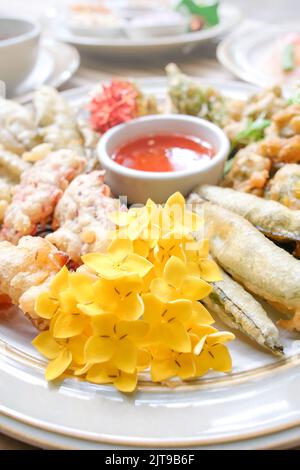 Des fleurs tropicales comestibles frits, des feuilles et des légumes servis sur une assiette blanche se trouvent sur la table en bambou. Une alimentation saine. Vue de dessus. Gros plan. Banque D'Images