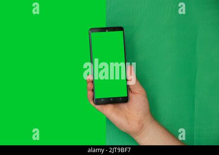 La main d'un homme sur fond vert contient un téléphone portable avec un écran vert, un modèle avec un téléphone, un écran vert, une photo avant et après la coupe Banque D'Images