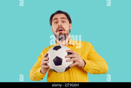 Studio photo de drôle timide gars dans la chemise tenant le ballon de football avec l'expression de visage effrayée Banque D'Images