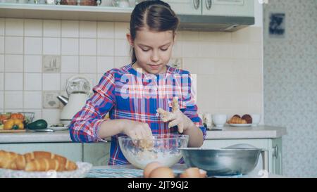 Petite fille cuisant de la pâte et nettoyant les mains souriant dans la cuisine à la maison. Elle veut suprise sa mère avec des biscuits cuits au four Banque D'Images