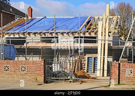 Construction d'un bâtiment de bungalow compact contenant des éléments de remplissage. Les travaux sur les murs de bordure de briques avant sont en cours sur les poutrelles et les échafaudages de toit en Angleterre Banque D'Images